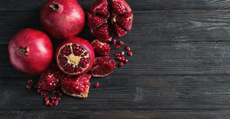 Ripe pomegranates and seeds on wooden background, flat lay with space for text